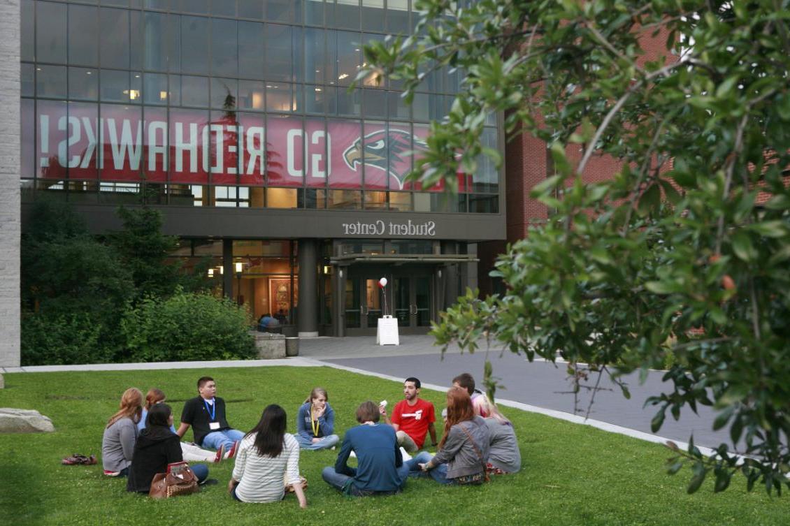students seated in a circle on lawn outside Student Center